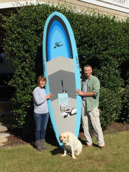 Paddleboard winners Kevin Durocher and Pam Van Velsor pose with their dog, Largo, with the paddleboard they won from the Surfside Shrimp Boil.